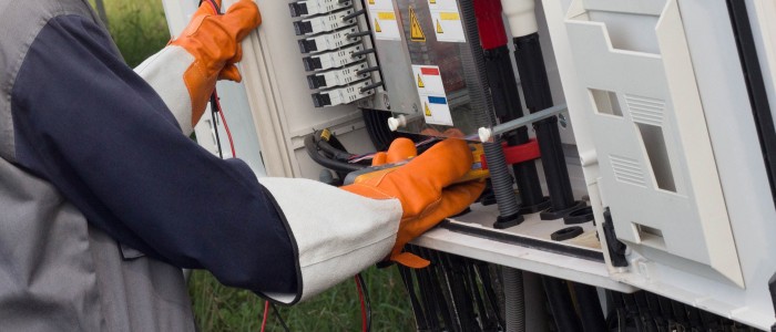 A person wearing orange gloves opening up a breaker box.