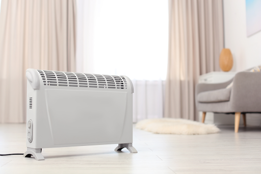 A white space heater sits safely in the middle of a cream colored living room.